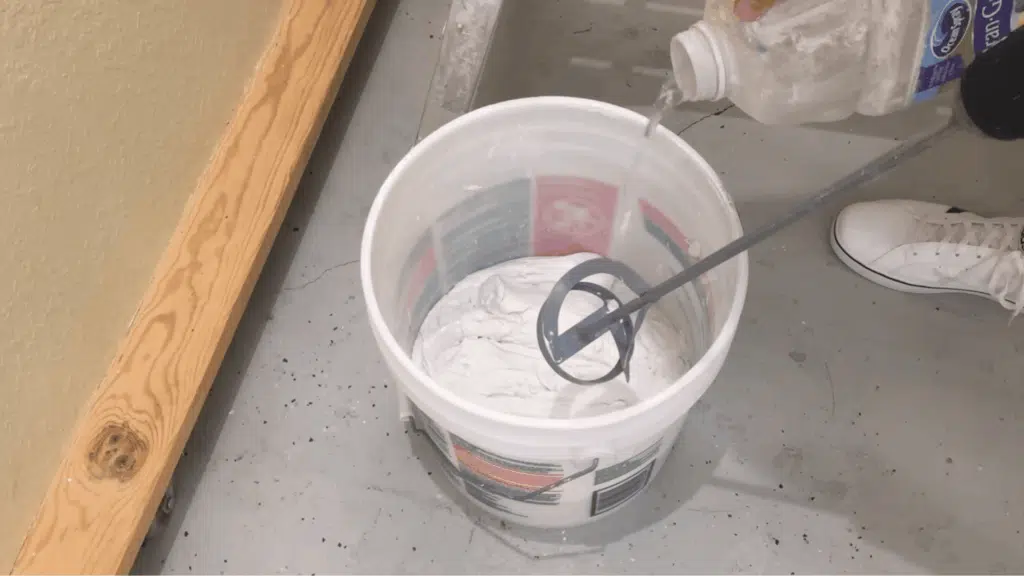 person adding water to joint compound and stirring until it reaches a smooth, yogurt-like consistency for skim coating.