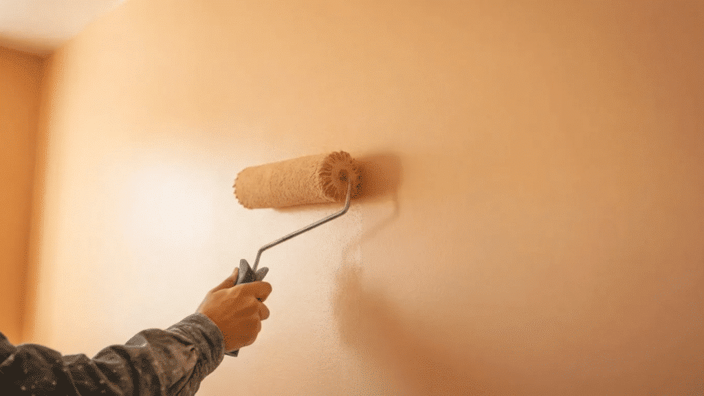 person applying a smooth coat of paint to an interior wall using a roller, showing even coverage and clean finish