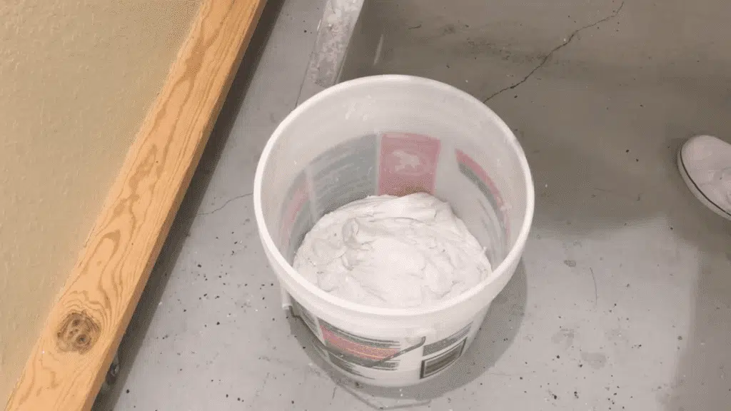 person dividing joint compound into two portions in separate buckets, preparing to mix it for skim coating