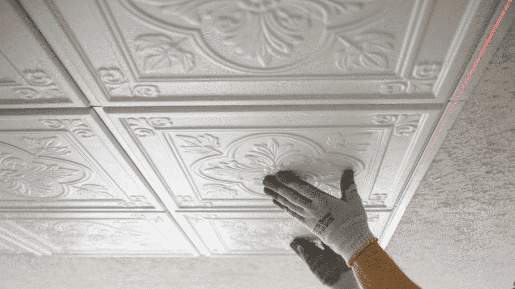 person installing decorative white ceiling tiles over textured ceiling wearing gloves