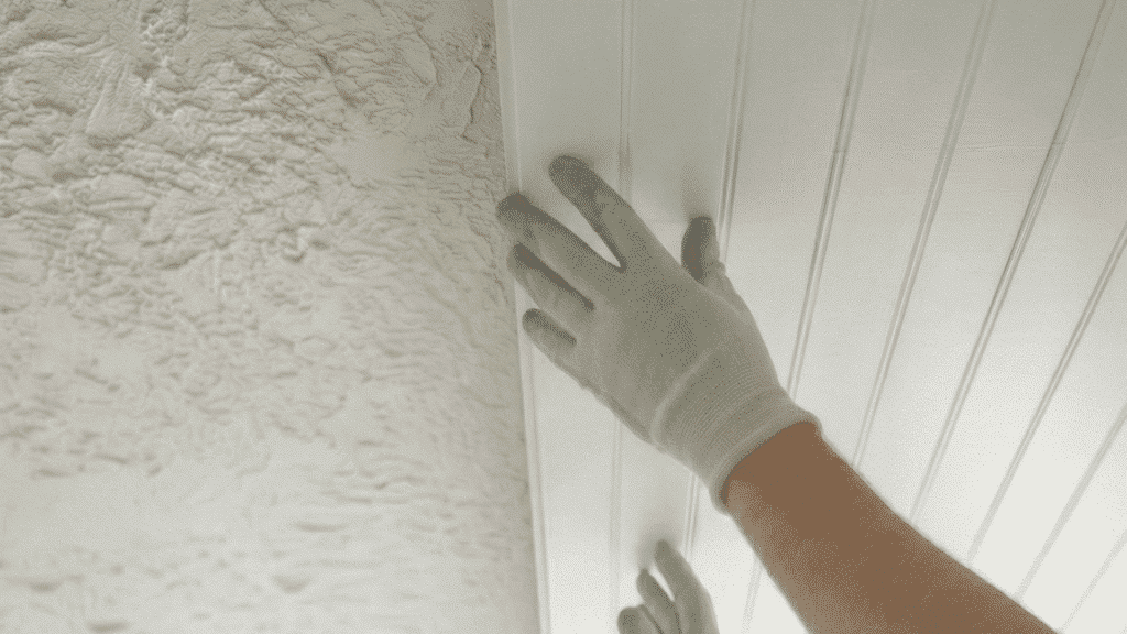 person installing white beadboard ceiling panel over textured ceiling while wearing gloves