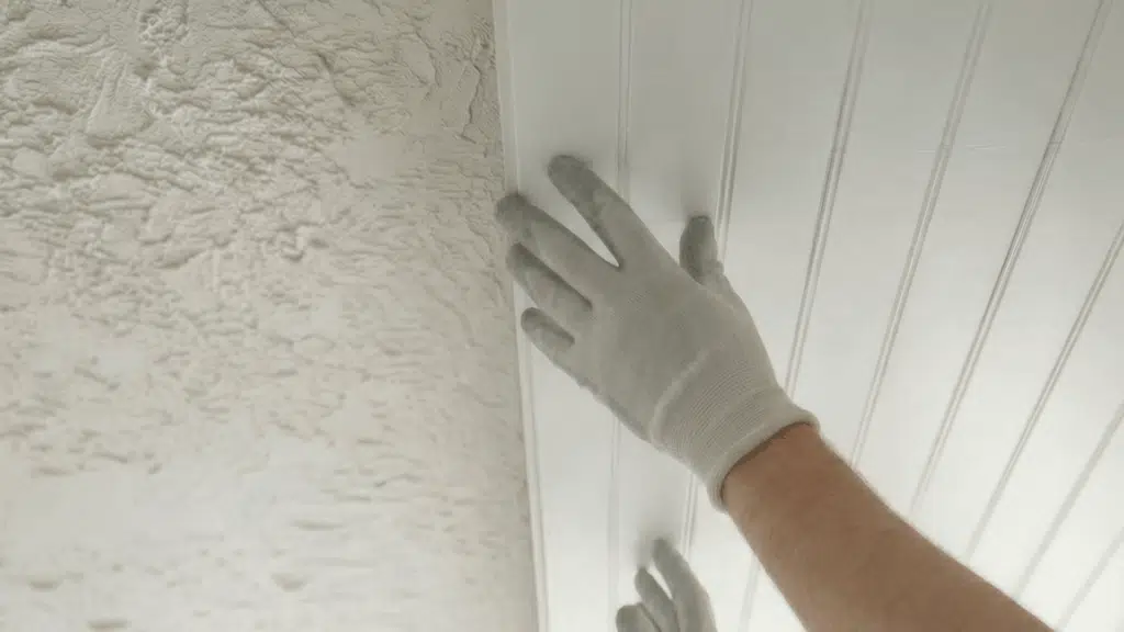 person installing white beadboard ceiling panel over textured ceiling while wearing gloves