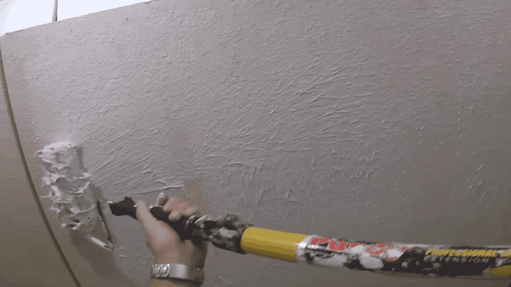 person rolling joint compound onto the wall with a paint roller, applying it in an even motion for a smooth layer.