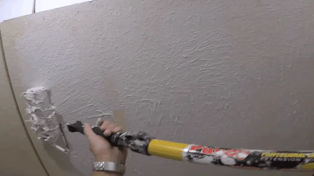 person rolling joint compound onto the wall with a paint roller, applying it in an even motion for a smooth layer.