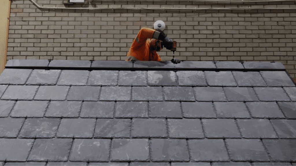 securing ridge slate tiles with drill and fixings at roof peak during final step of slate roofing installation process