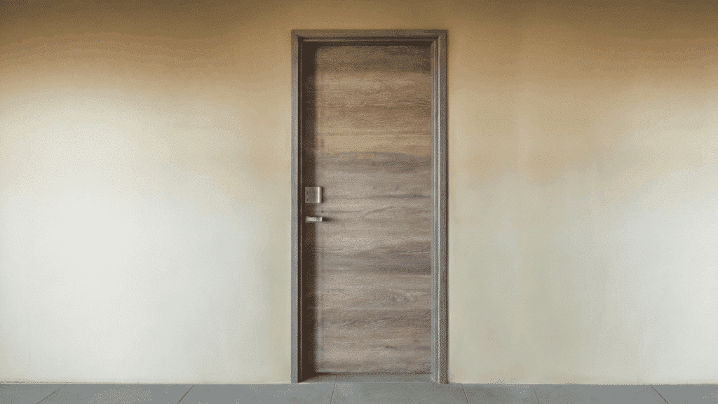 single prehung door with wooden finish and silver lever handle installed in a plain beige interior wall