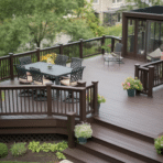 spacious brown deck with a dining table, comfortable seating, and decorative plants, surrounded by greenery.