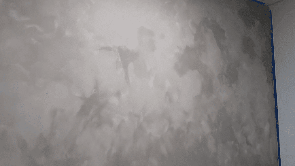 textured beige wall with mottled finish next to edge taped with blue painter’s tape, showing decorative paint effect in progress