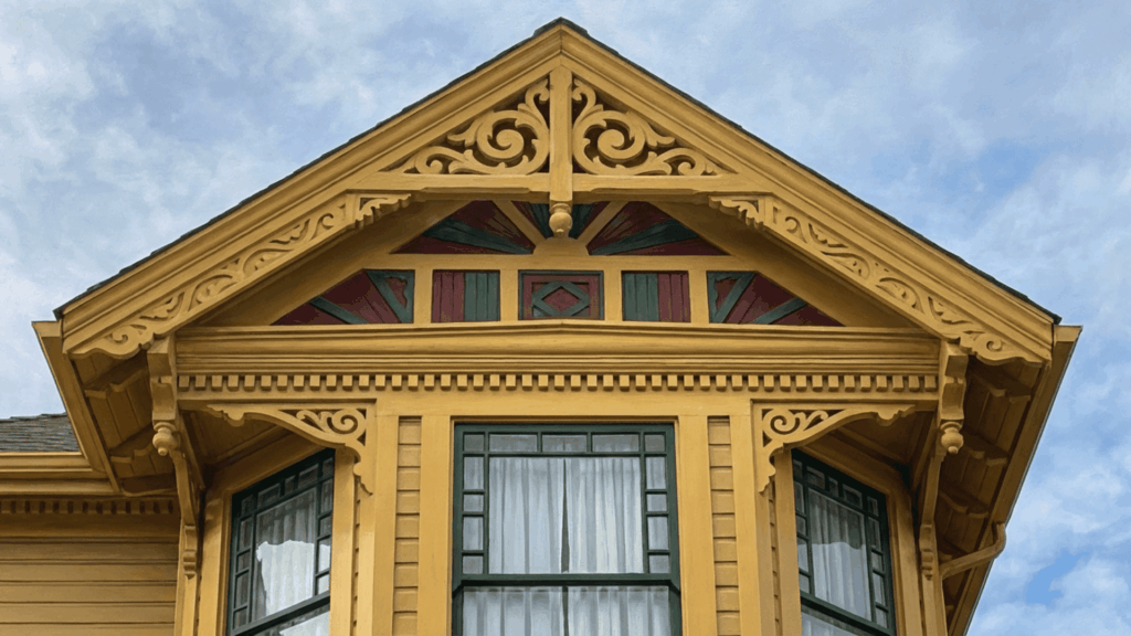 victorian home open eaves with ornate yellow carved woodwork decorative brackets and green red painted panels against a cloudy sky