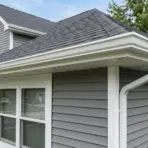 view of house roof edge showing fascia soffit and gutter with gray siding and shingles on suburban home