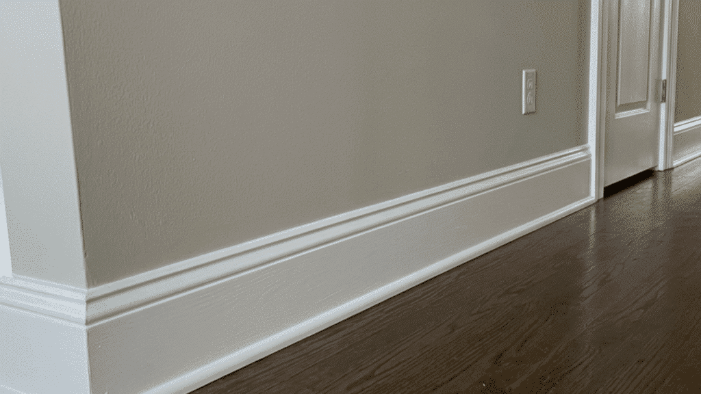 white baseboard trim along hallway wall with dark wood flooring, neutral walls, and doorway leading to another room