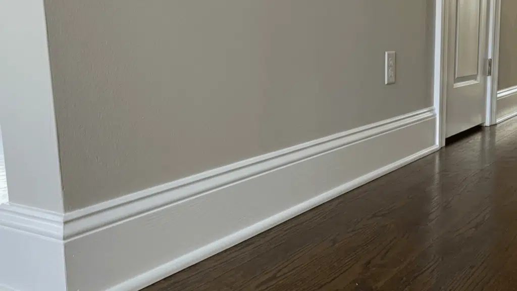 white baseboard trim along hallway wall with dark wood flooring, neutral walls, and doorway leading to another room