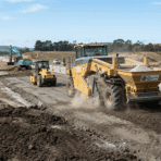 yellow soil reclaimer mixing lime into earth followed by a roller compactor on a highway construction site.
