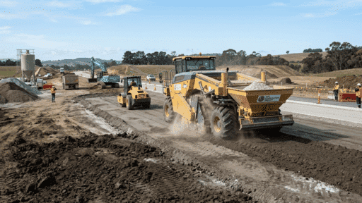 yellow soil reclaimer mixing lime into earth followed by a roller compactor on a highway construction site.