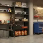 Red classic car parked in organized garage with shelving, tools, and equipment on walls