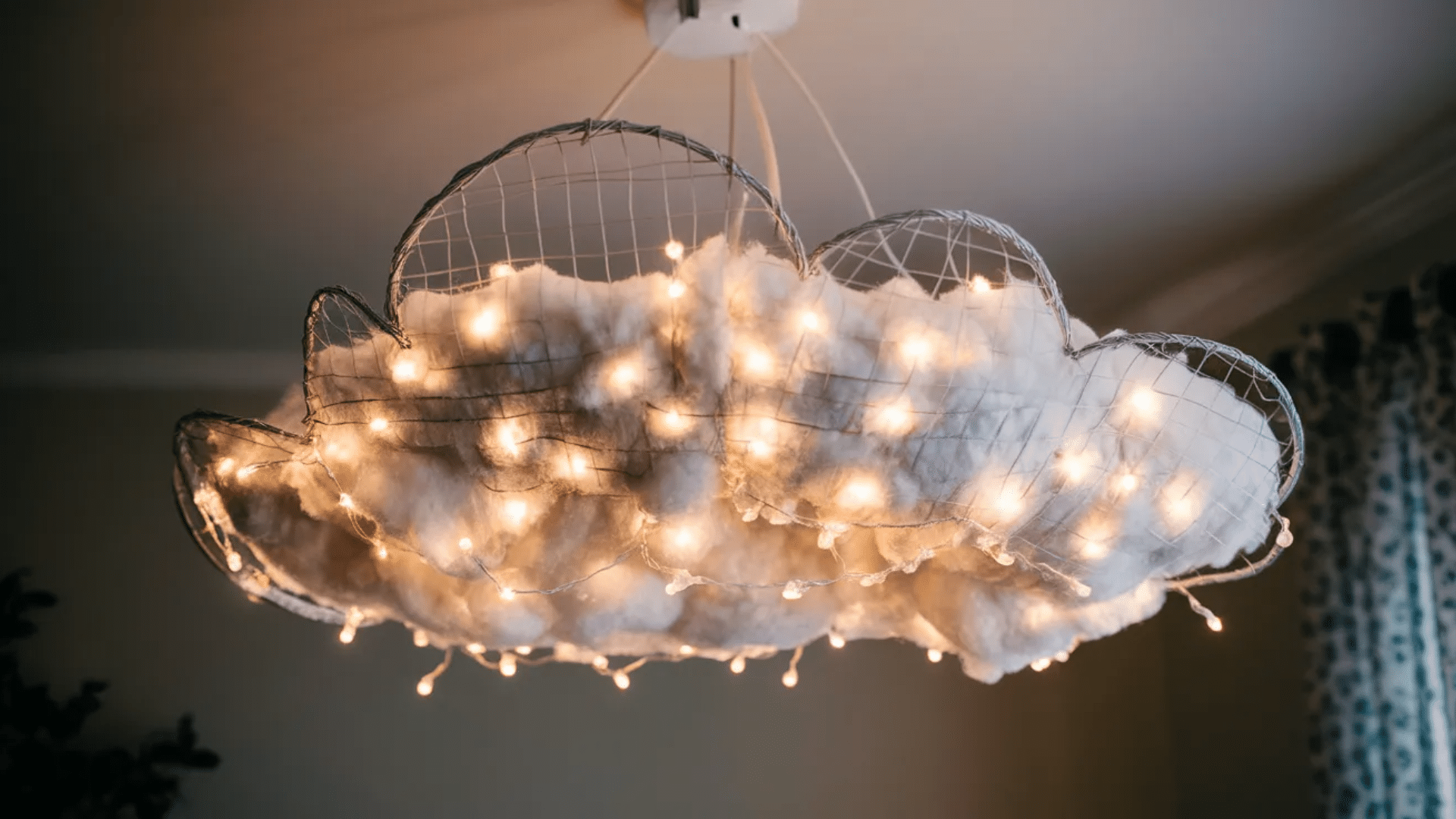 a cloud-shaped light fixture made of wire and cotton, with string lights embedded, creating a cozy, whimsical ambiance in a room.