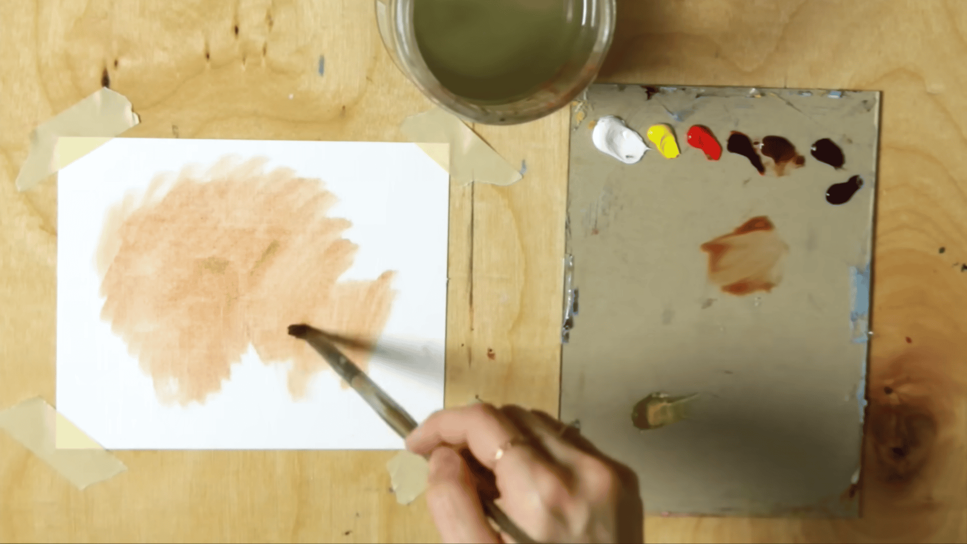 a filbert brush applying diluted burnt sienna across oil painting paper to create a warm toned base before painting
