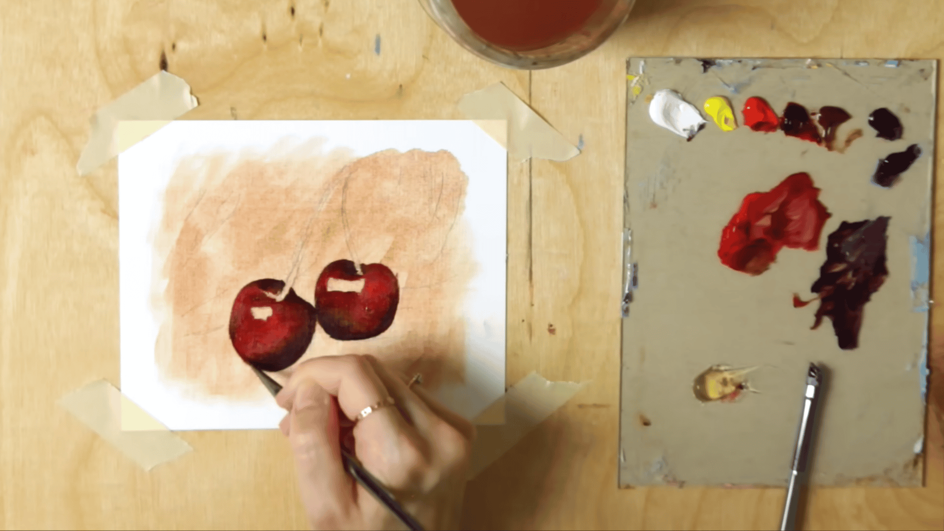 a liner brush building deep red and dark shadow colours onto cherries showing layered depth in an oil painting study