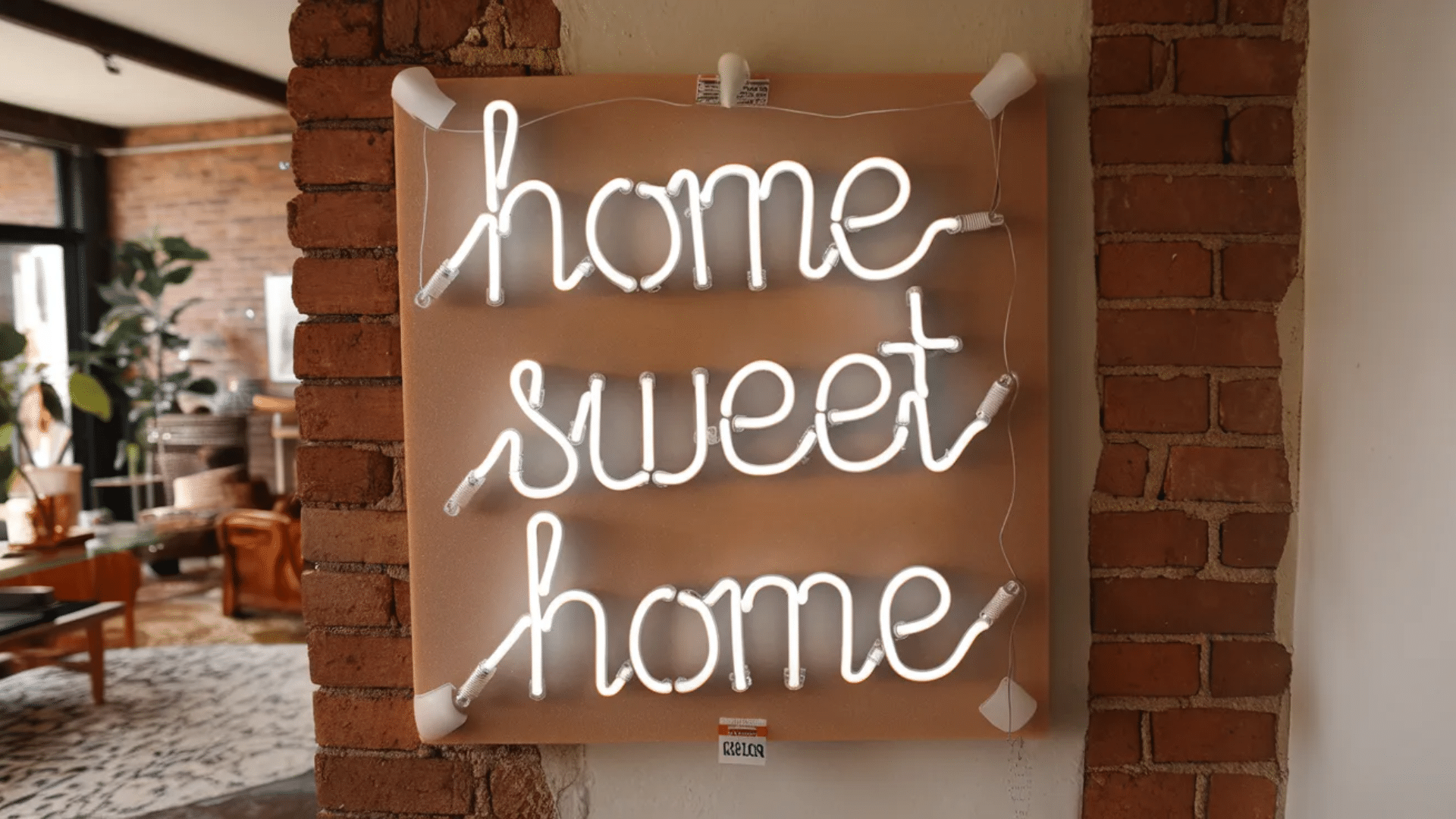 a neon light sign reading home sweet home mounted on a tan board, hanging on a brick wall in a cozy, rustic interior space.