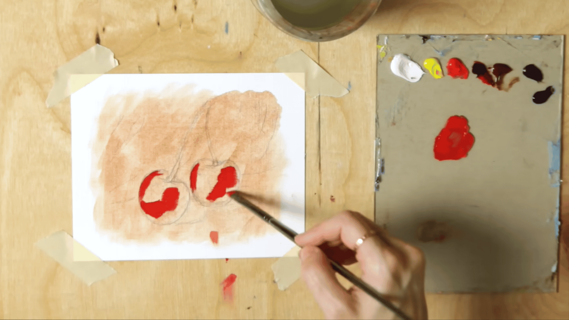 an angle brush applying bright cadmium red paint onto the sketched cherry shapes on a toned oil painting surface