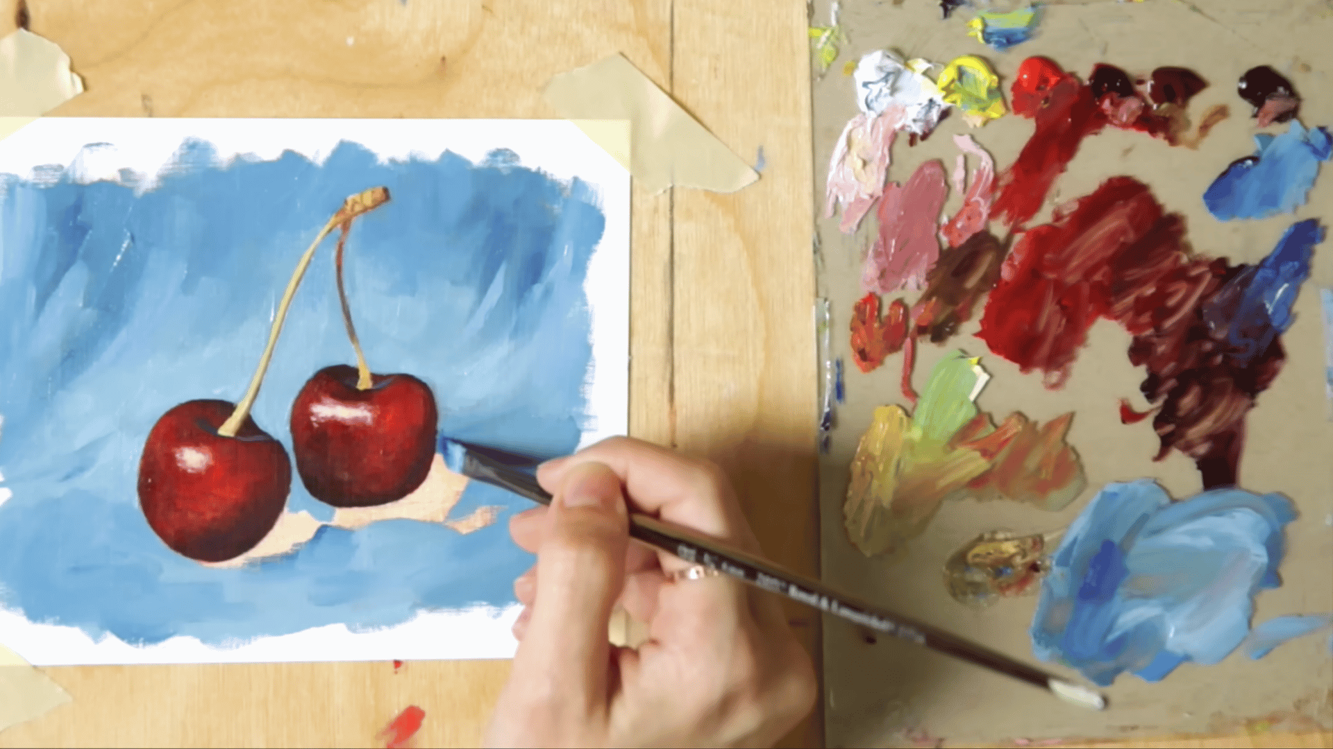 an angle brush filling in a blue fabric background around painted cherries completing the oil painting composition