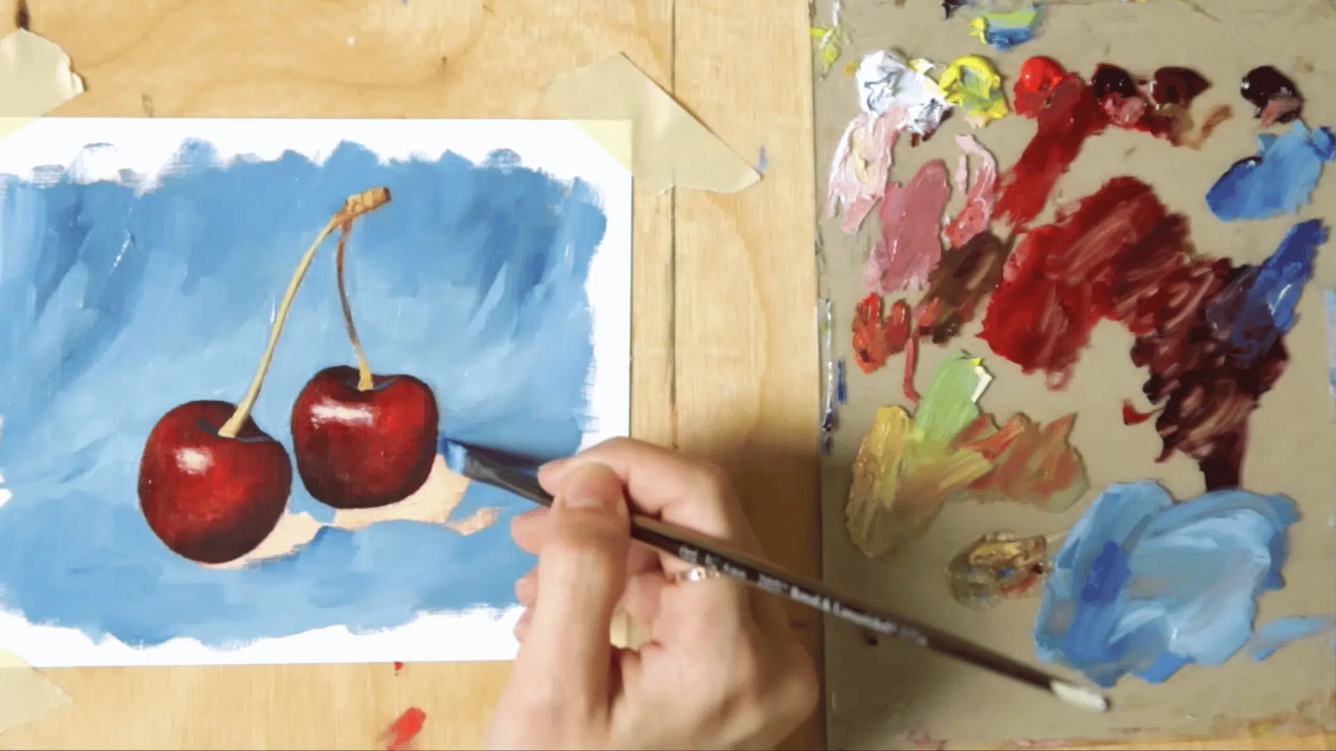 an angle brush filling in a blue fabric background around painted cherries completing the oil painting composition
