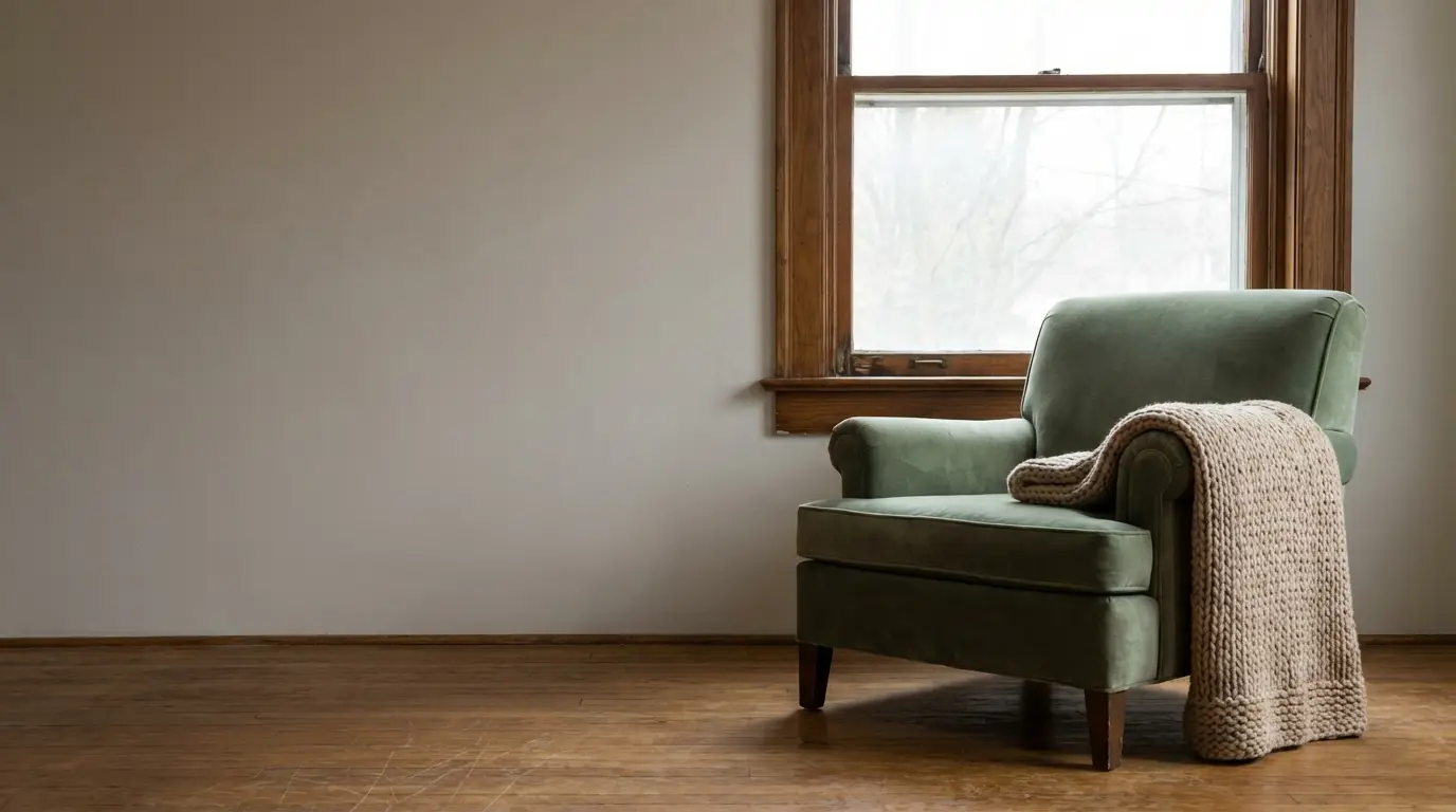 Green armchair with beige knit throw beside large window in minimalist living room