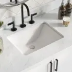 Marble bathroom countertop with black faucet, candle, and small plant in glass vase