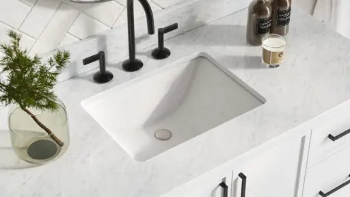 Marble bathroom countertop with black faucet, candle, and small plant in glass vase