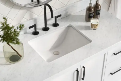 Marble bathroom countertop with black faucet, candle, and small plant in glass vase