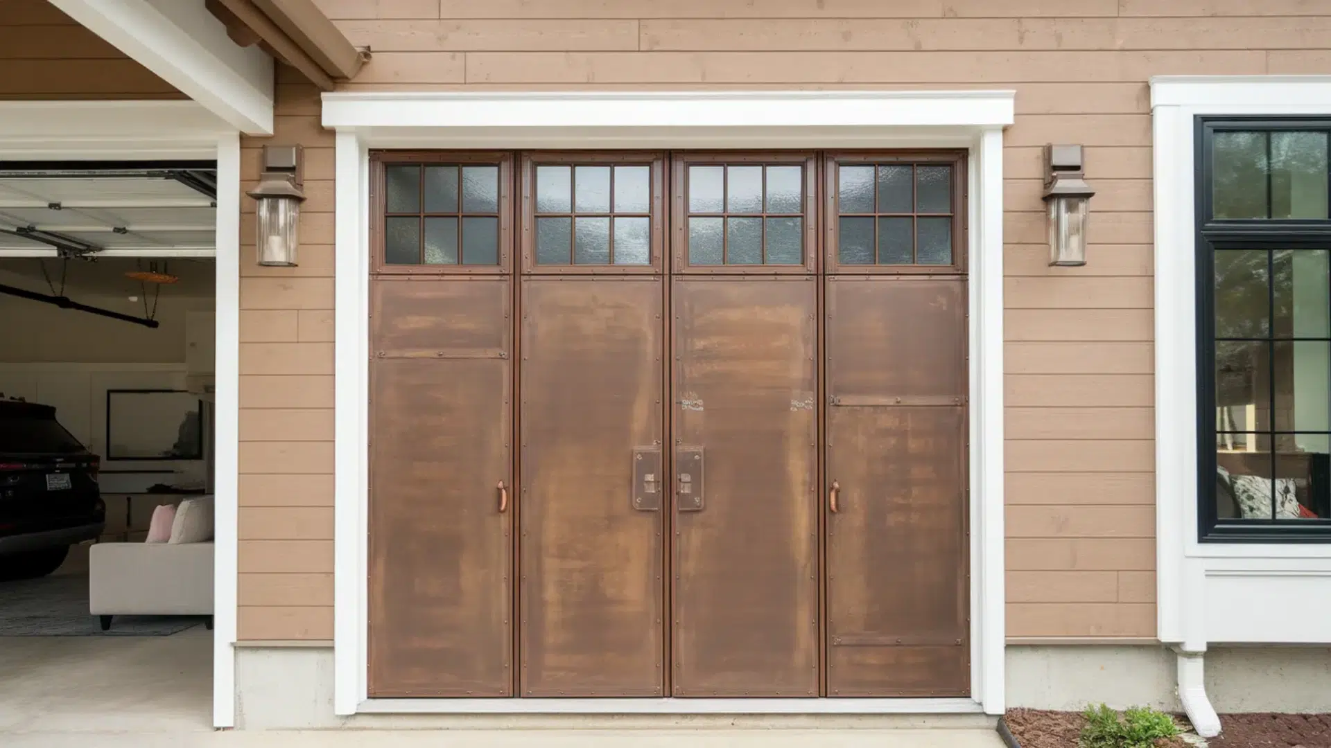 brown metal garage door with small window panels at the top is set into a beige house exterior with wall-mounted lantern lights on each side.
