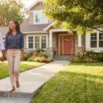Couple walking on pathway in front of house with landscaped garden and large tree