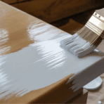 close-up of hand painting wooden surface with white paint using brush, showing DIY furniture refinishing process