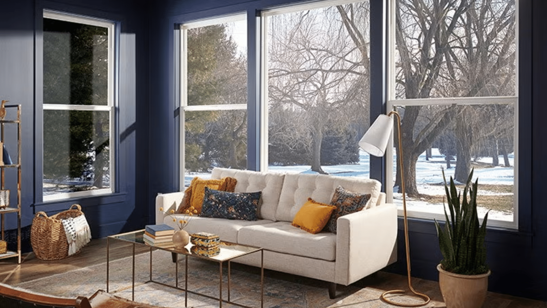 cozy living room with large windows, sofa with colorful cushions, indoor plants, and winter landscape visible outside