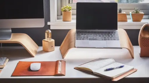 Laptop and desktop on wooden stands in modern workspace with notepad and potted plants