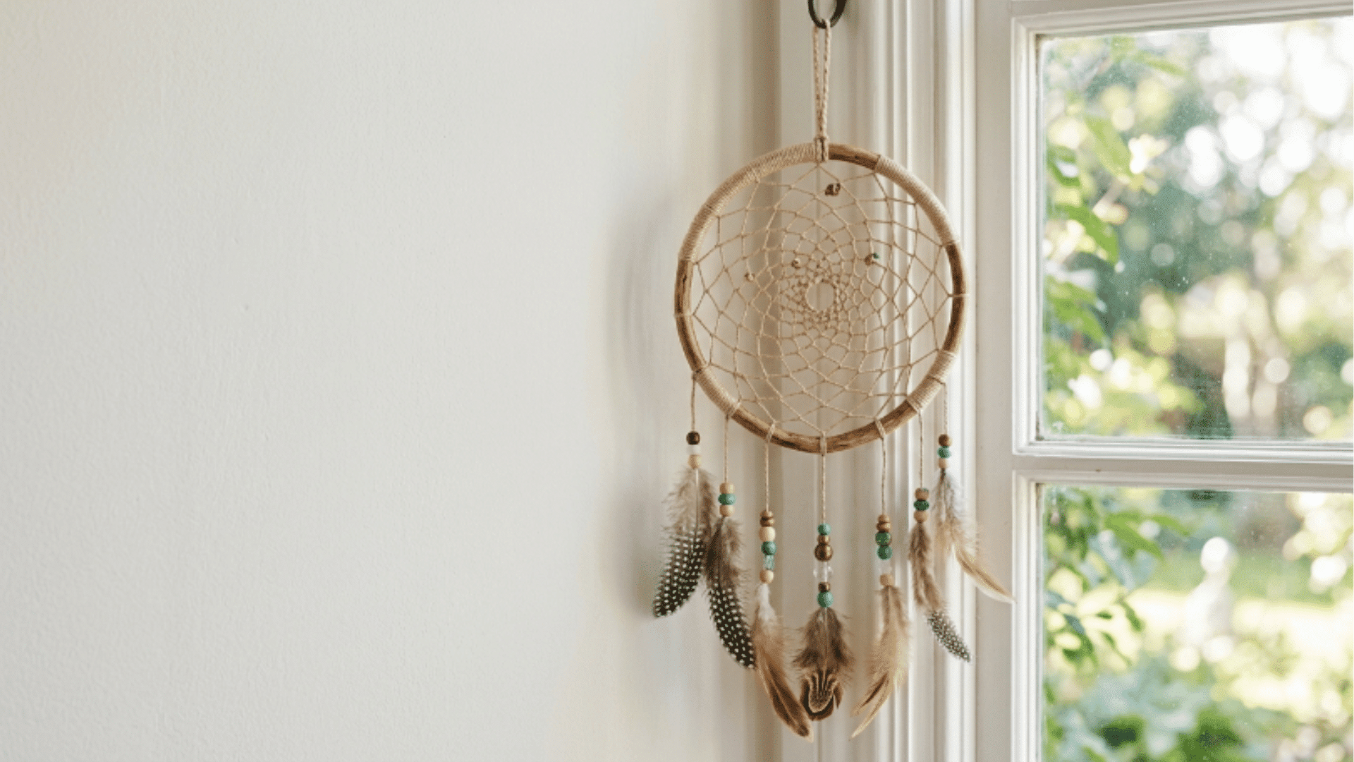 dreamcatcher with woven thread pattern and beads hanging near window with soft light and minimal background
