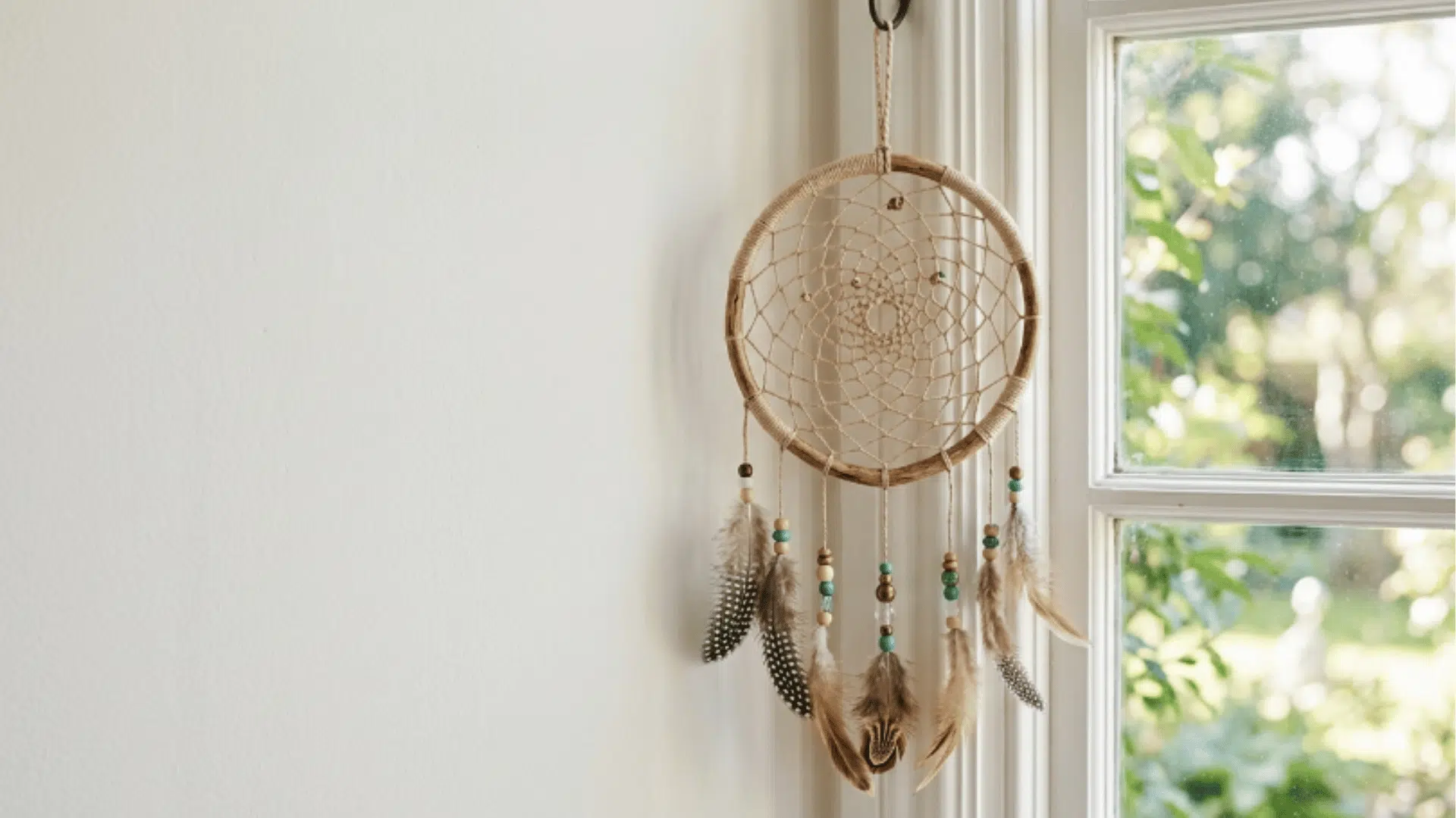 dreamcatcher with woven thread pattern and beads hanging near window with soft light and minimal background
