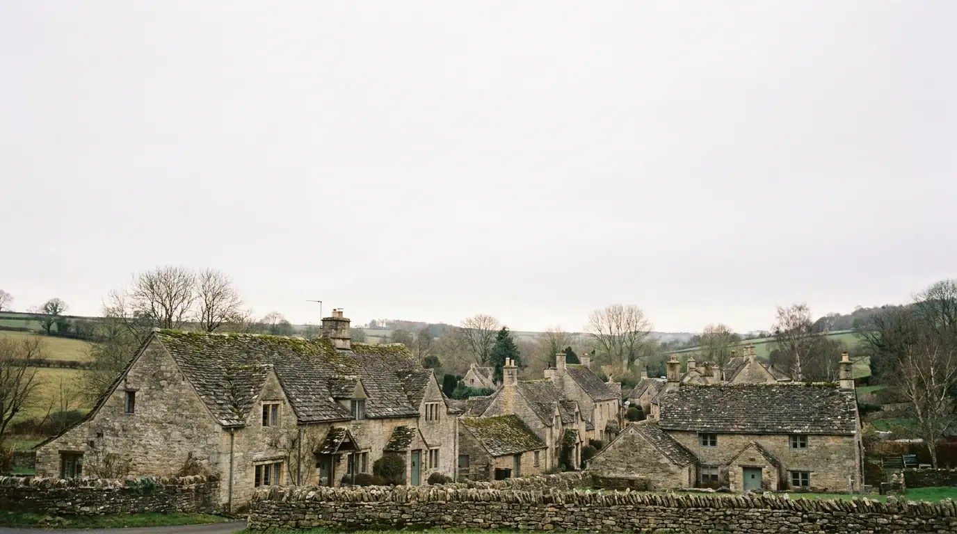 Stone cottages with moss-covered roofs in a rural village setting under overcast sky