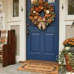 fall front door decor with wreath, pumpkins, lantern, and welcome mat.