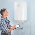 Maintenance worker inspecting a wall-mounted water heater with clipboard in hand