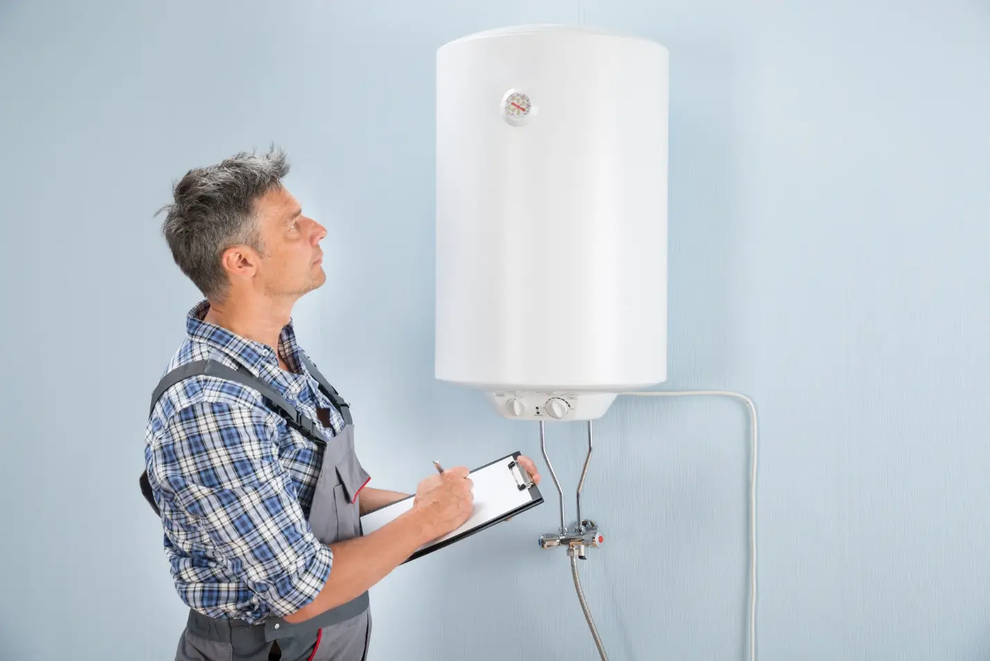 Maintenance worker inspecting a wall-mounted water heater with clipboard in hand