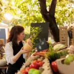 Woman examining butternut squash at an outdoor market stall with fresh produce