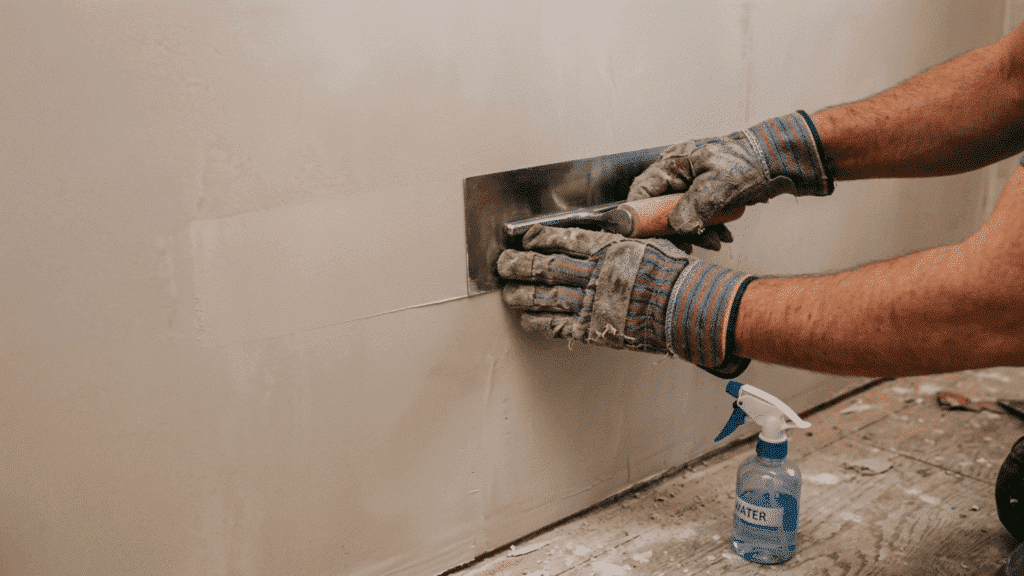 gloved hands polishing a nearly finished plaster wall surface using a clean steel trowel with light controlled pressure