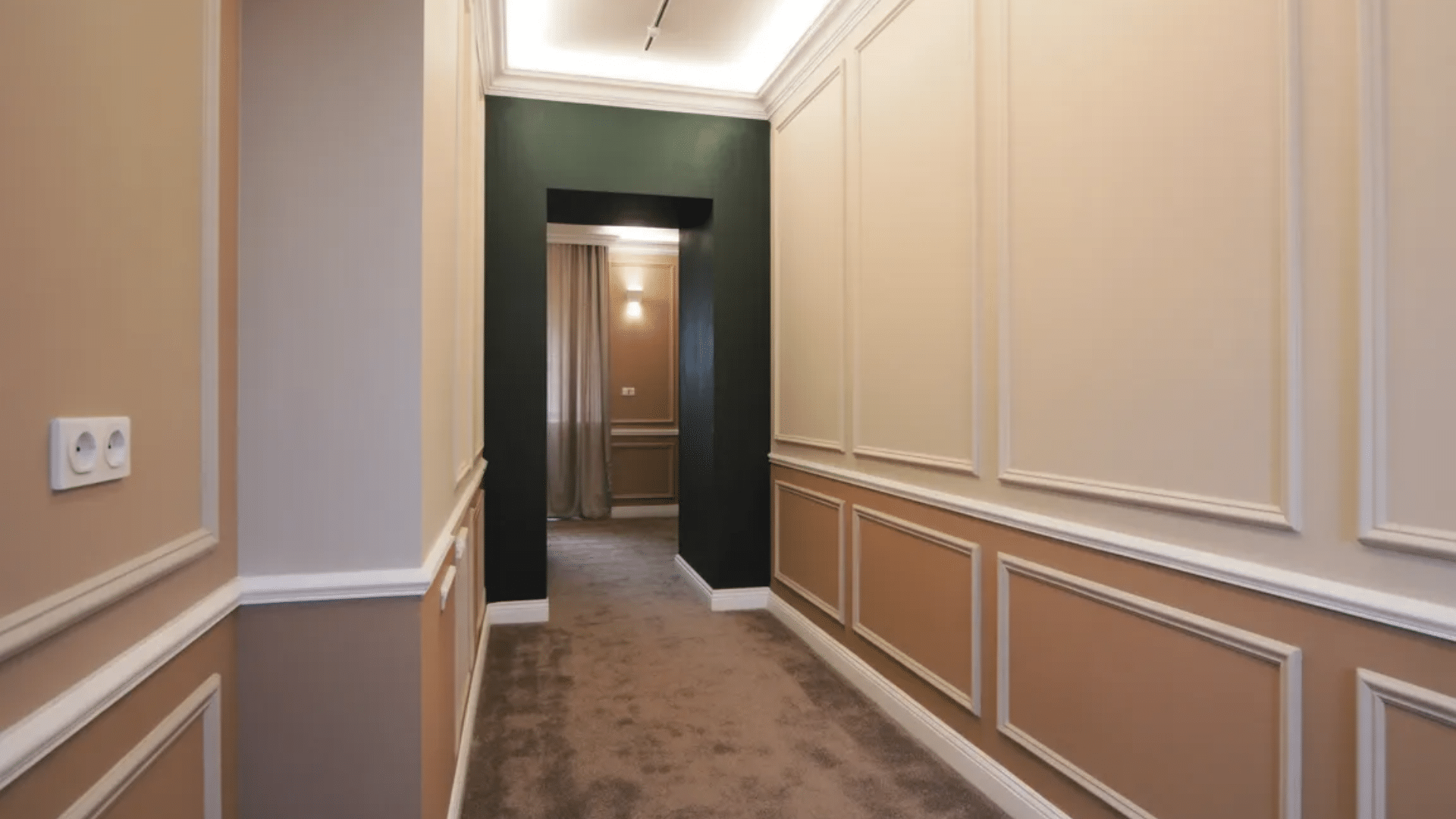 hallway with decorative wall molding paneling in neutral tones leading to doorway with darker accent wall and carpeted floor