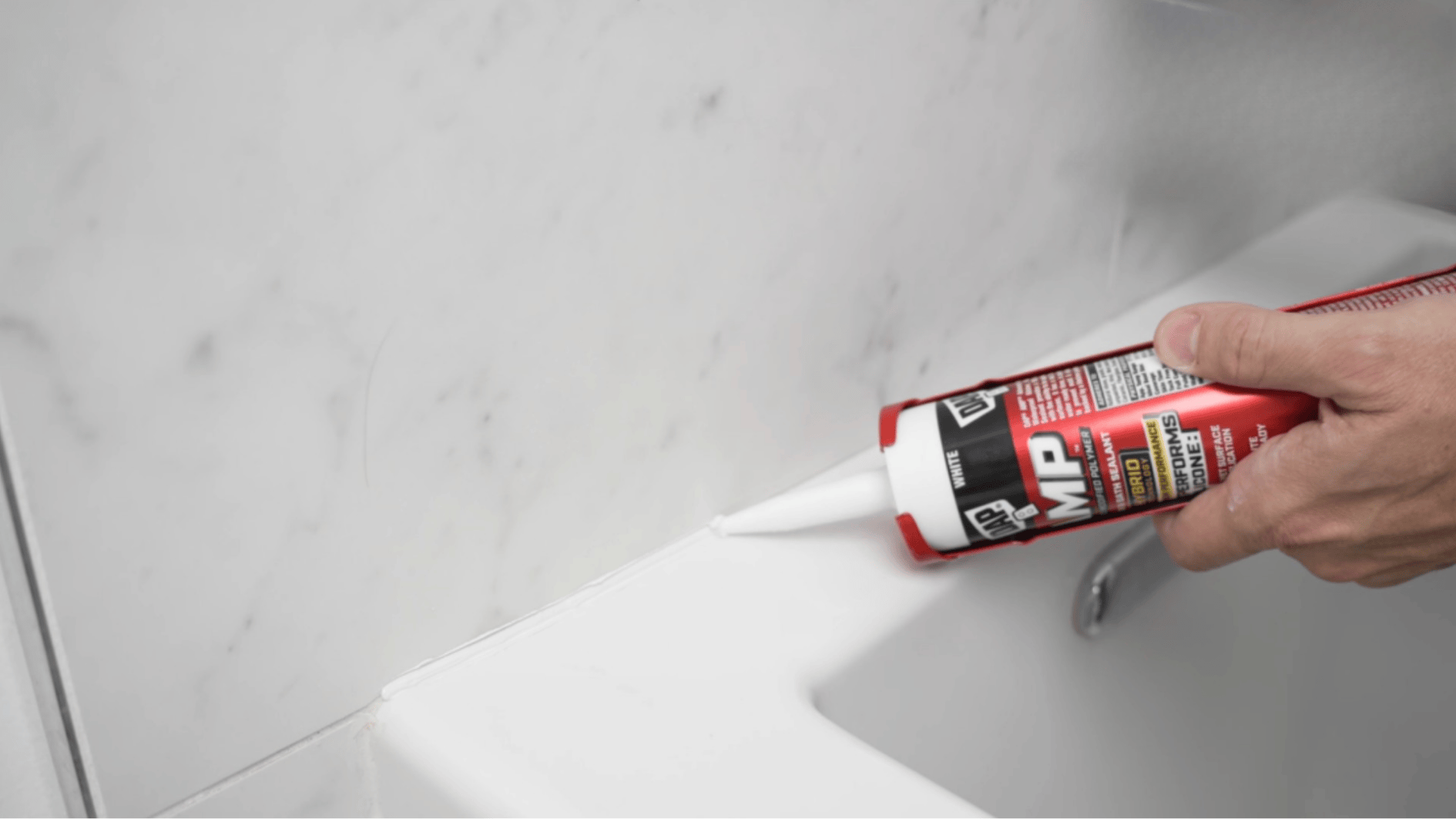 hand applying white caulk along edge where tub meets wall for sealing joint in bathroom (1)