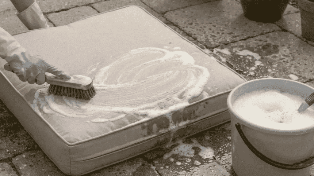hand scrubbing outdoor cushion with soap and brush on patio floor.