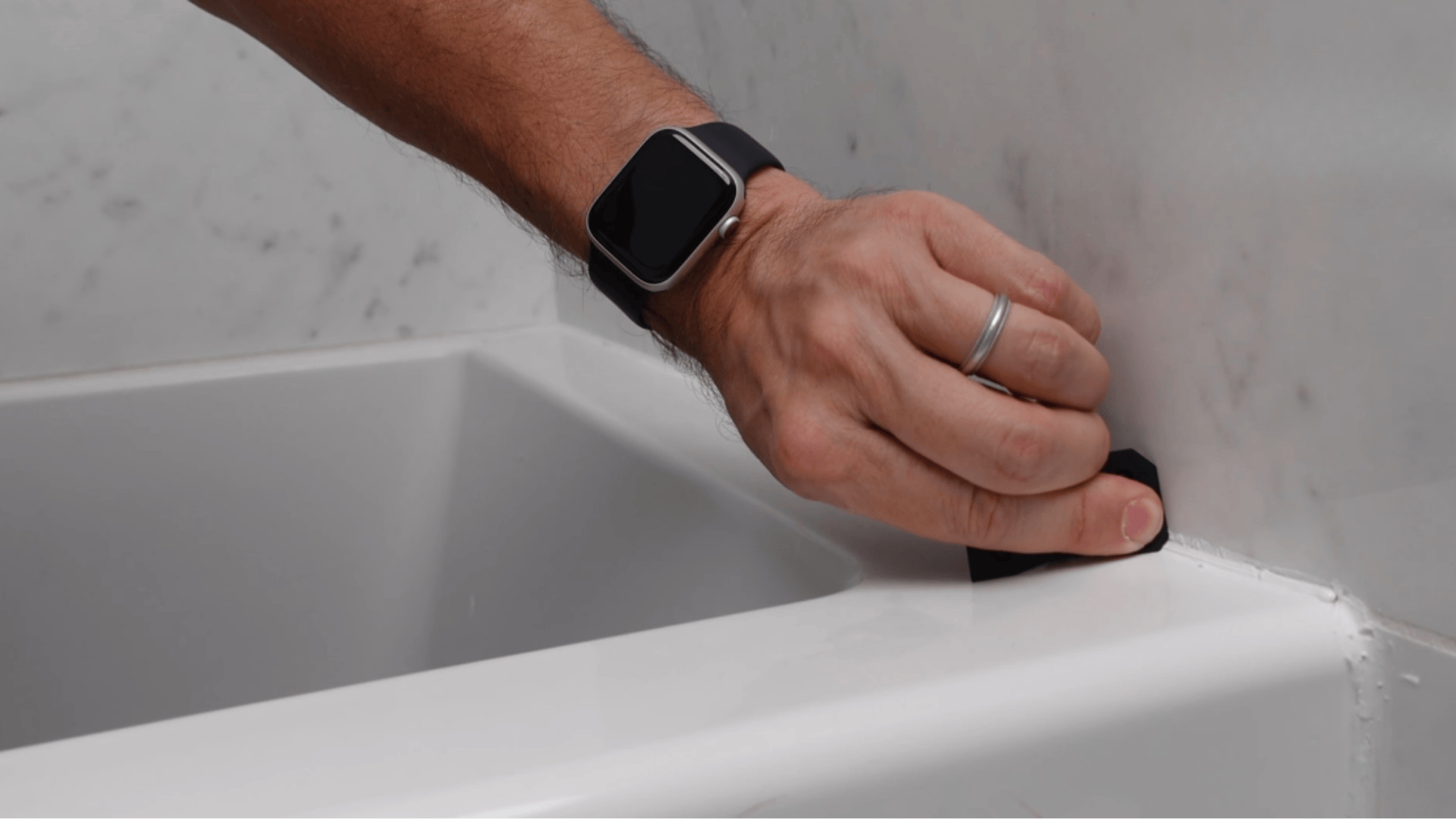 hand smoothing fresh caulk bead along tub edge with tool for clean finish in bathroom (1)