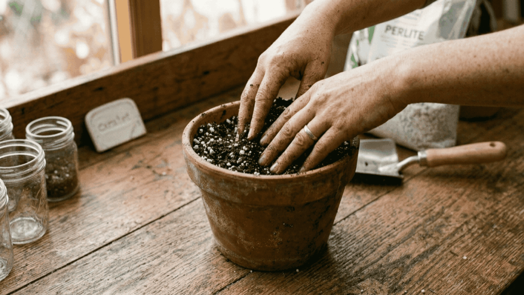 hands mixing fresh potting soil with perlite inside a terracotta pot on a wooden surface with drainage holes visible nearby