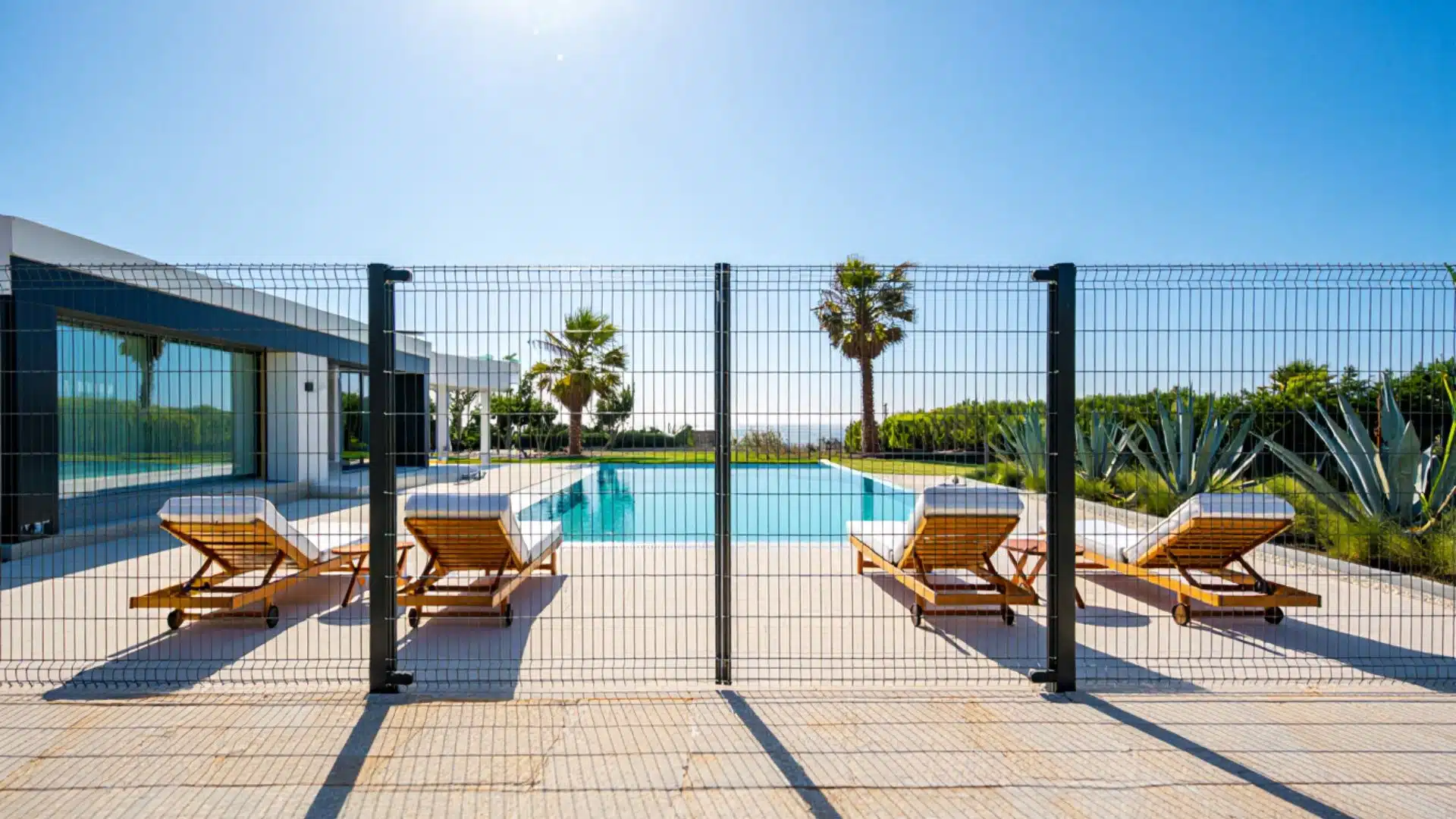 hog wire pool fence with black metal posts enclosing a modern backyard swimming pool with lounge chairs and palm trees