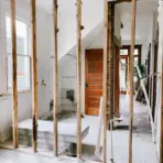 Indoor renovation scene with exposed wooden studs and unfinished walls in a bright hallway